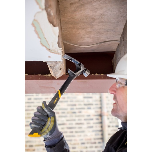 STANLEY FMHT51367-2 claw hammer with black and yellow handle used for demolition work by a gloved hand.