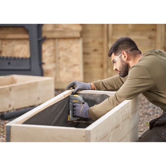 STANLEY FMHT6-70868 staple gun being used to fasten fabric inside a wooden planter box outdoors.