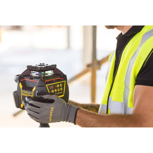 Photo of STANLEY FMHT77447-1 laser level device held by worker wearing safety vest and gloves.