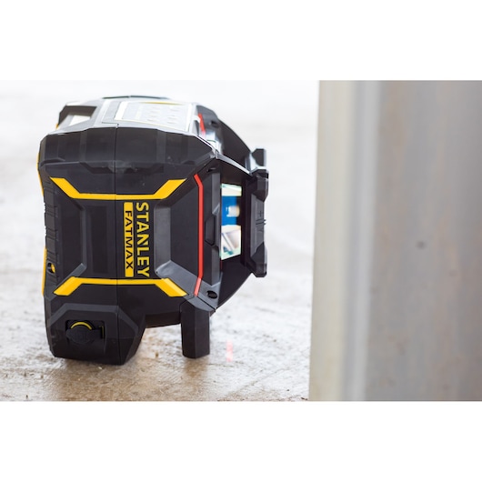 STANLEY FMHT77447-1 laser level device, black with yellow accents, side angle, on a construction floor.