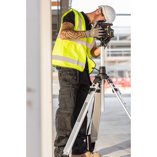 STANLEY FMHT77449-1 construction laser level on tripod, used by worker in safety vest and helmet.