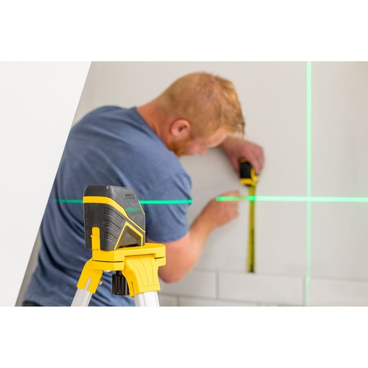 STANLEY FMHT77586-1 laser level on tripod projecting green lines, person measuring wall.