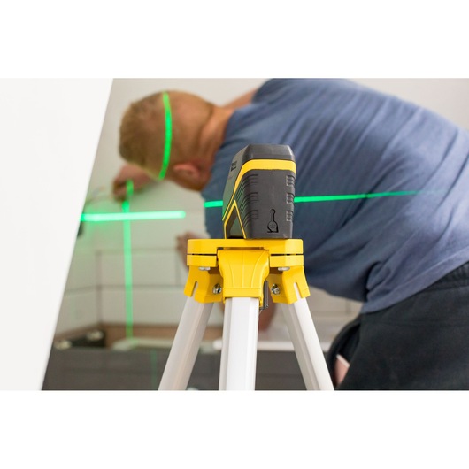 Photo of STANLEY FMHT77595-1 laser level on tripod projecting green lines in interior workspace.