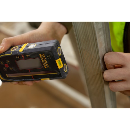 Photo of STANLEY FMHT77652-0 digital detector held against metal surface, construction context.