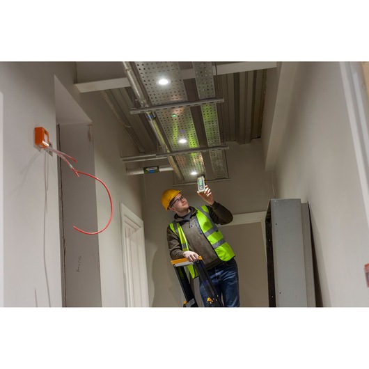 STANLEY FMHT77653-0 detector used by worker in safety vest under ceiling wiring, indoor photography.