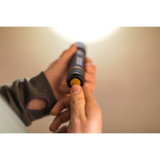 STANLEY FMHT81511-0 flashlight in hand, showing yellow button being pressed, close-up photography.