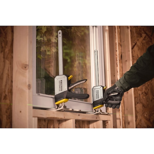 STANLEY FMHT83550-1 metal bar clamp used to secure a window frame during installation on a wooden structure.