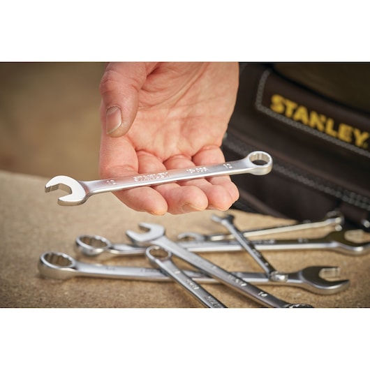 STANLEY FMMT13040-0 spanner held in hand, with several silver wrenches on a work surface, close-up photography.