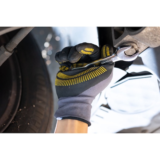 STANLEY FMMT13109-0 wrench used by gloved hand tightening a bolt near a car wheel, close-up.