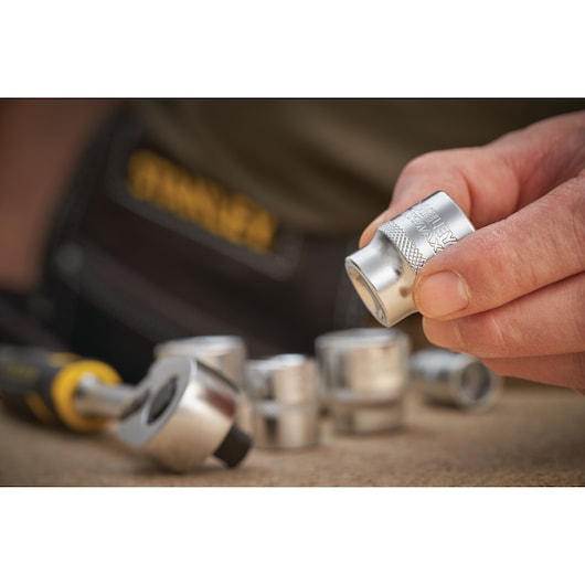 STANLEY FMMT17222-0 socket held in hand, with ratchet and other sockets on work surface, close-up photo.