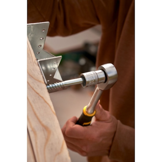 Photo of STANLEY FMMT82827-1 ratchet socket wrench in use on bolt, with wooden board and metal bracket.