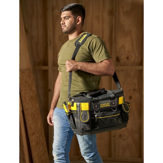 Photo of STANLEY FMST1-70749 tool bag with yellow accents, carried by person with shoulder strap.