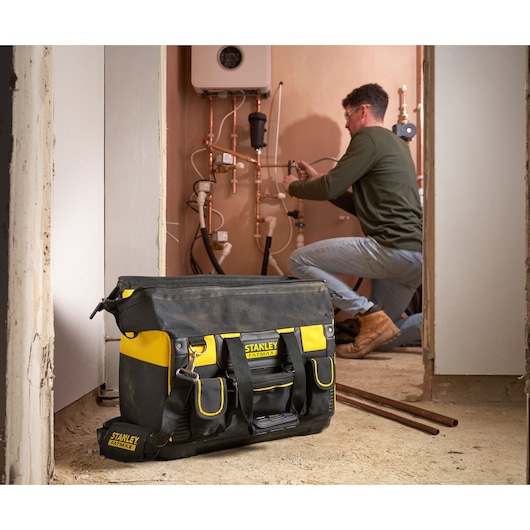 STANLEY FMST1-71180 tool bag in black and yellow with external pockets, shown on a construction site floor.