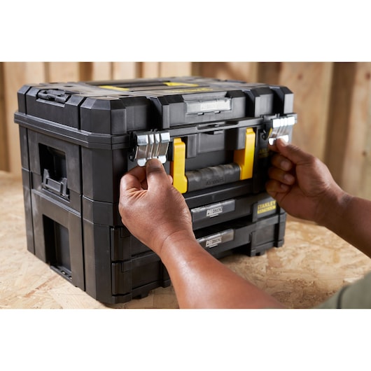 STANLEY FMST1-71981 black stackable toolbox with metal latches, hands opening the front, product in use.