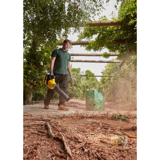 Photo of STANLEY SFMCBLB76B leaf blower used outdoors to clear debris from ground, green bag in background.