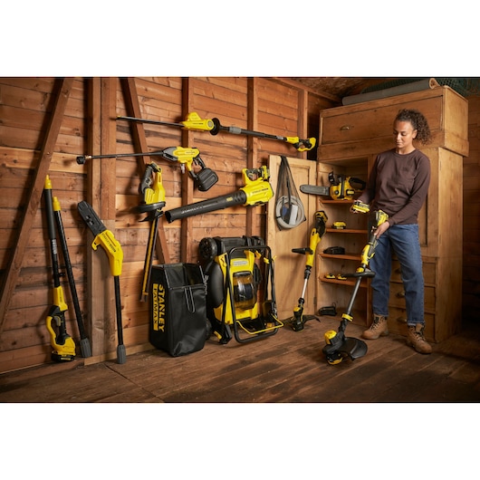 Photo of STANLEY SFMCCS630M1 garden tools collection displayed in wooden shed, person holding string trimmer.
