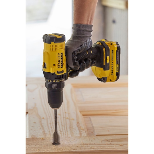 STANLEY SFMCD700C2K cordless drill in use, yellow and black, drilling wood with large drill bit.