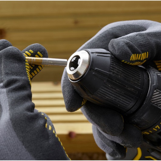 STANLEY SFMCD700C2K drill close-up with gloved hands inserting a metal bit, outdoor setting.
