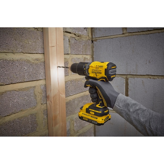 STANLEY SFMCD715D1A cordless drill being used to drill into wood on a brick wall.