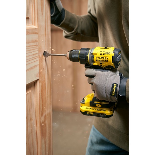 Stanley SFMCD720B cordless drill in use drilling into wood, side angle photography.