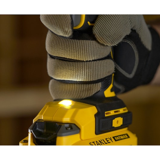 Photo of gloved hand gripping STANLEY SFMCD720D2K cordless drill with LED light on, close-up view.