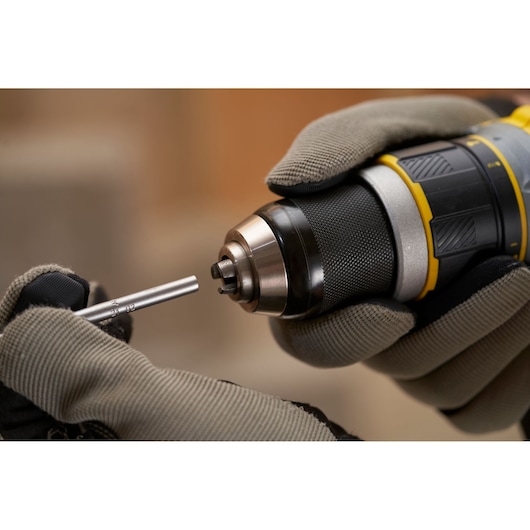 Photo of STANLEY SFMCD721B cordless drill being fitted with a metal bit, close-up, gloves visible.