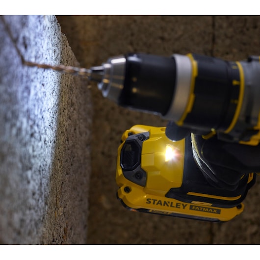 STANLEY SFMCD721D2K drill driving into a concrete wall, yellow FATMAX branding visible, close-up view.