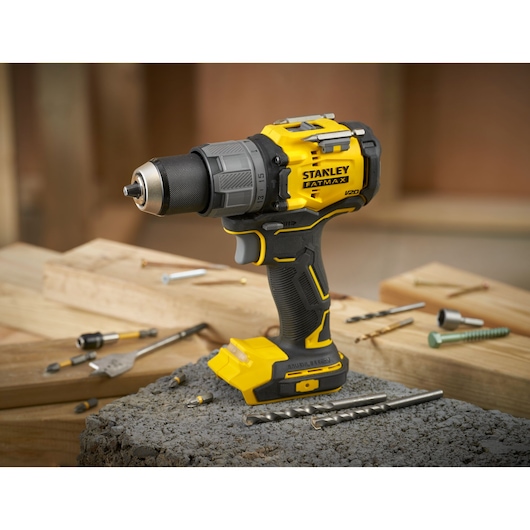 STANLEY SFMCD726B cordless drill in yellow and black, side angle, shown with drill bits on wood and concrete.