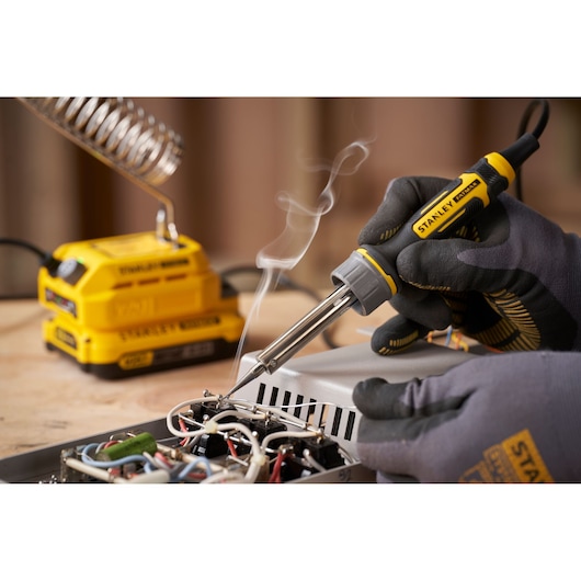 Photo of STANLEY SFMCE040B soldering iron in use, with gloved hand soldering electronic components on a circuit board.