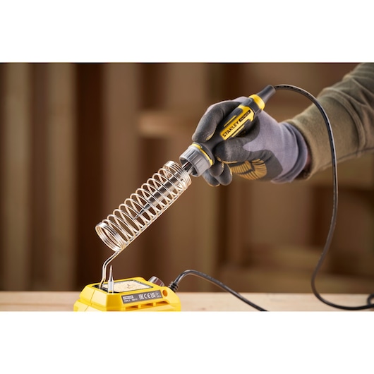 STANLEY SFMCE040B soldering iron held by gloved hand near yellow base, close-up photography.