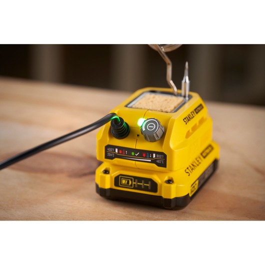 STANLEY SFMCE040B soldering station with yellow body, control knob, and LED indicator on wooden surface, front angle.