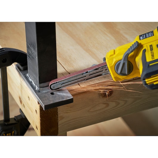 STANLEY SFMCE210D2 cordless belt file grinding metal corner on wooden workbench, side angle view.