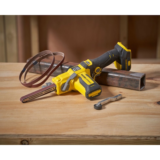 STANLEY SFMCE210D2 cordless belt file with sanding belt and wrench on wood surface, front angle.