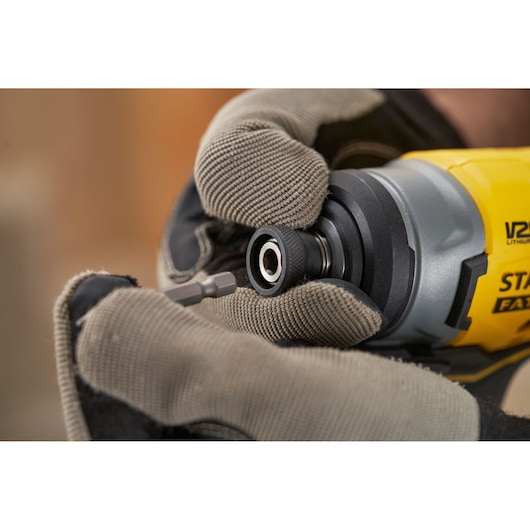 Close-up photo of gloved hands inserting bit into STANLEY SFMCF810B cordless impact driver, tool in use.