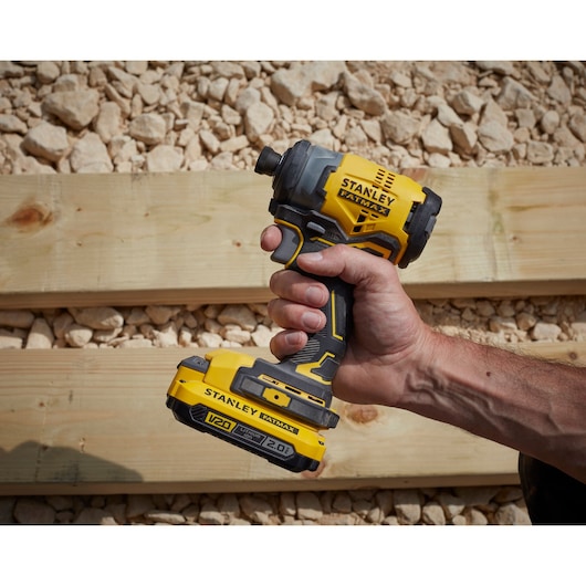 STANLEY SFMCF820D2K V20 cordless impact driver held in hand, yellow and black, outdoor setting.