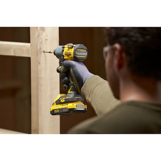 Photo of STANLEY SFMCF830B cordless impact driver being used on wooden frame, close-up side view.