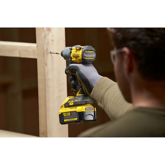 STANLEY SFMCF830B cordless impact driver in use, driving a screw into wooden studs, close-up view.