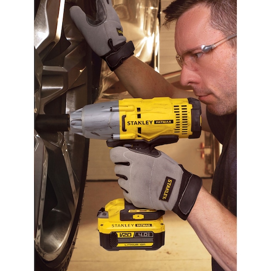 Stanley SFMCF900B cordless impact wrench used by gloved hands tightening a car wheel.