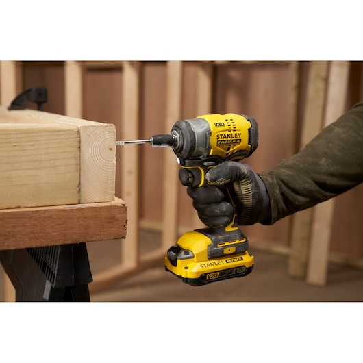 STANLEY SFMCF910B impact driver in yellow and black, drilling into wood, close-up side view.