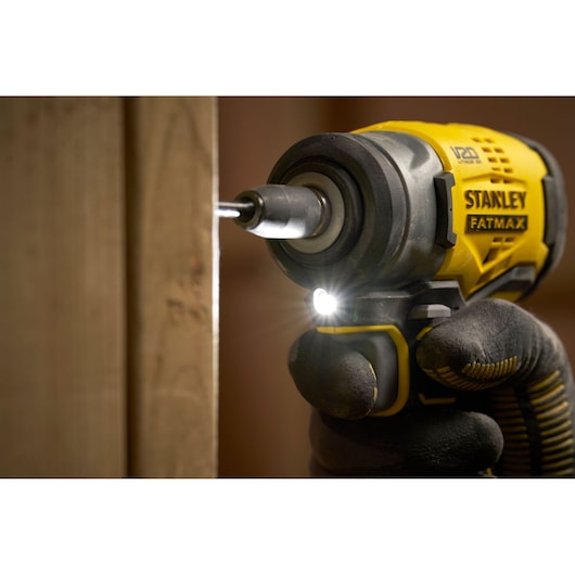 STANLEY SFMCF910B cordless impact driver in use, close-up with LED light on, driving screw into wood.