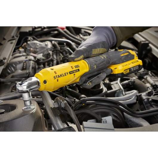 Photo of STANLEY SFMCF930B cordless ratchet tool in use tightening a bolt in a car engine compartment.