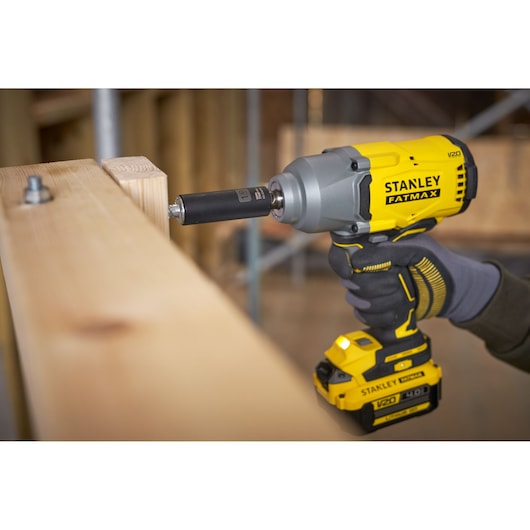 Photo of STANLEY SFMCF940B cordless impact wrench in use, driving a bolt into wooden beams.