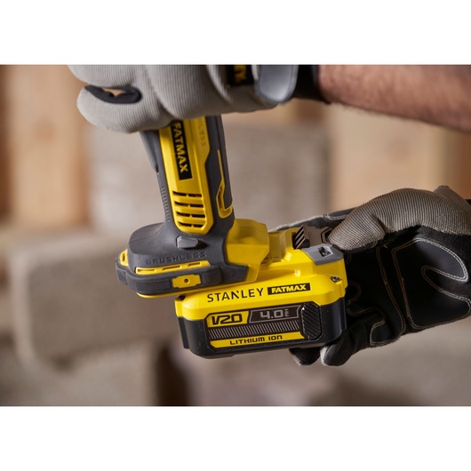 Stanley FATMAX SFMCG700B angle grinder with V20 4.0Ah lithium-ion battery, close-up held by gloved hands.