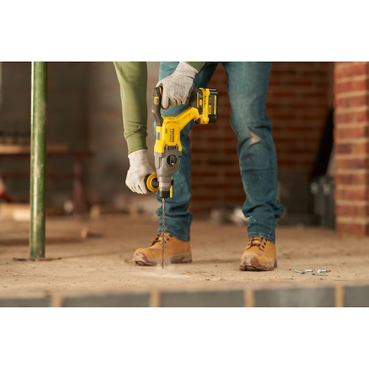 STANLEY SFMCH900M22 rotary hammer drill in use, drilling into concrete floor at construction site.