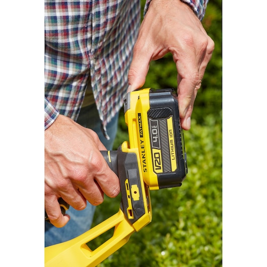 Photo of STANLEY SFMCHT855B V20 4.0Ah battery being attached to yellow cordless tool outdoors.