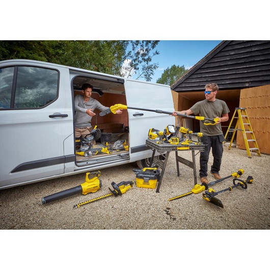 STANLEY SFMCHT855M1 garden tools set, various yellow power tools displayed outdoors near a van and work table.
