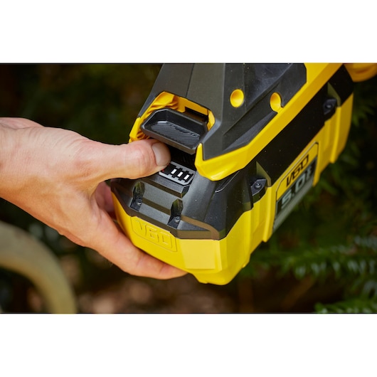 STANLEY SFMCHTB866B battery close-up with hand pressing release, yellow and black outdoor tool.