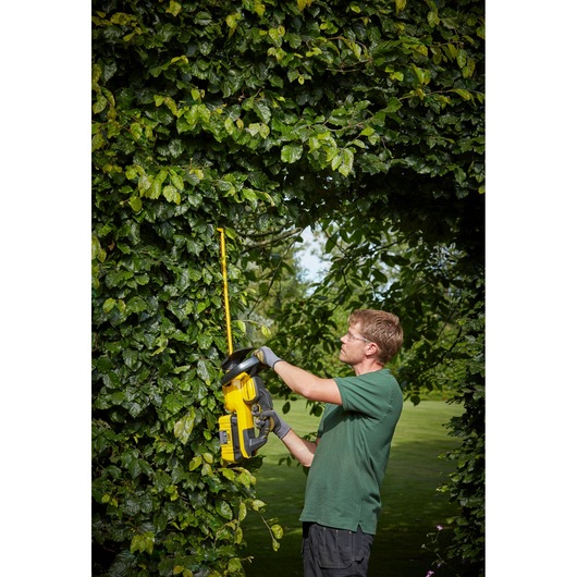 STANLEY SFMCHTB866B hedge trimmer in use outdoors, yellow and black tool cutting thick green hedge.