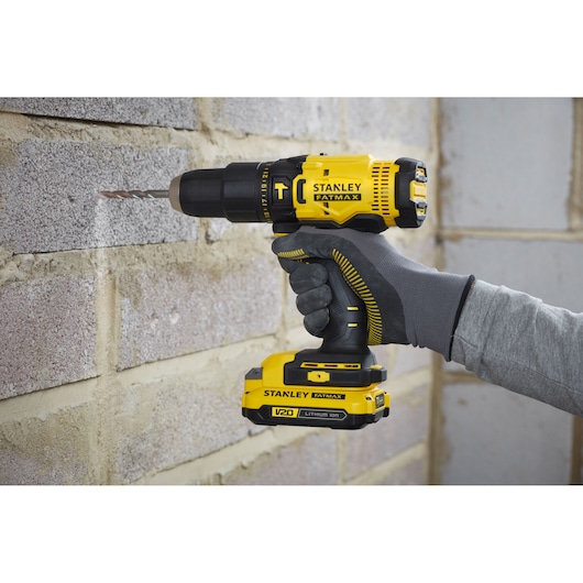 STANLEY SFMCK465D2S cordless drill driver in use drilling into a brick wall, close-up side view.