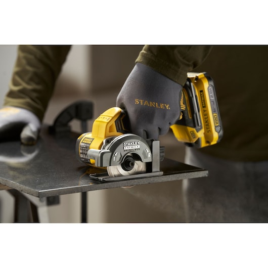 Photo of STANLEY SFMCM300B compact cordless circular saw cutting metal, worker wearing STANLEY gloves.